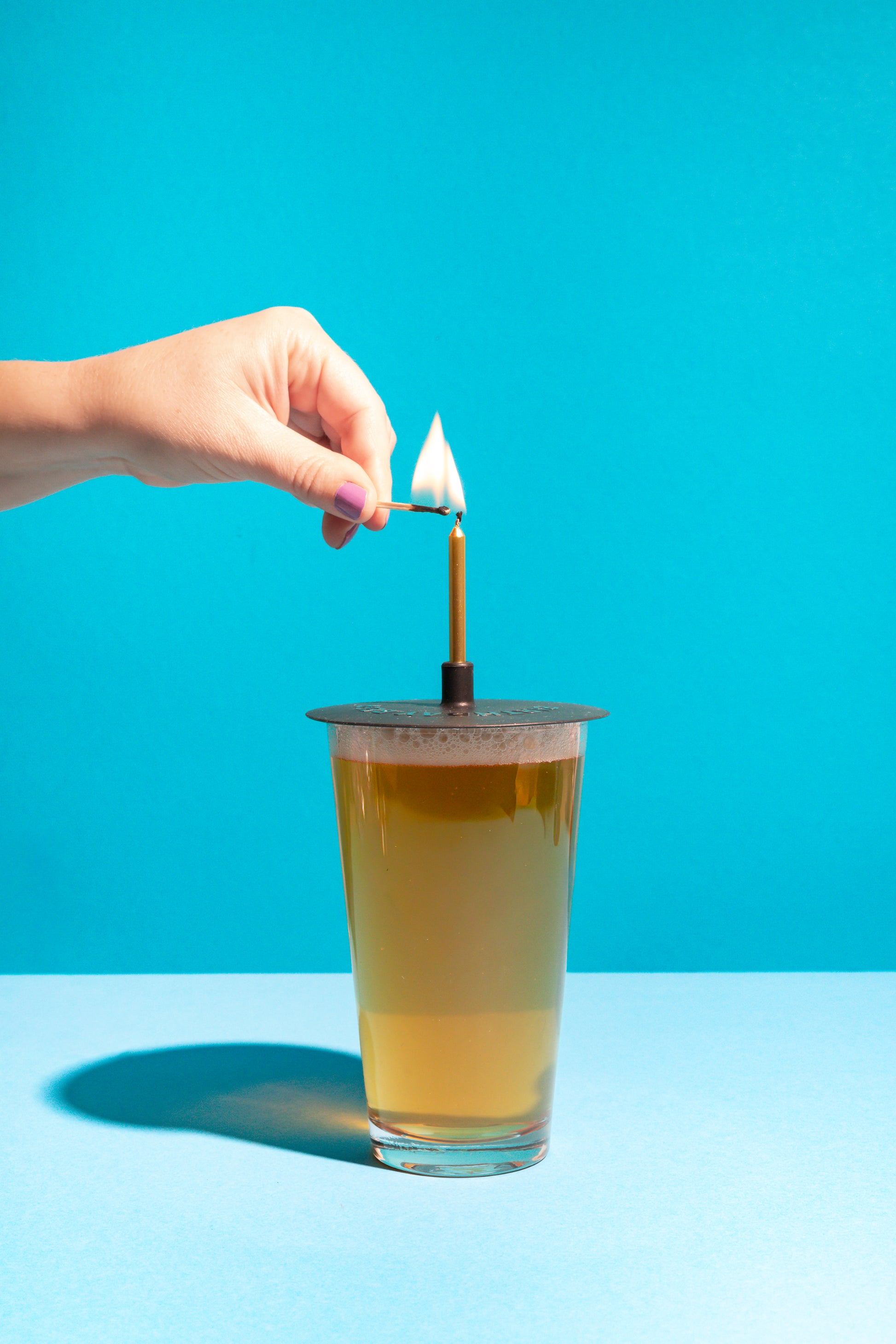 Hand lighting a candle on a glass of beer against a blue background